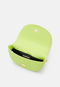 Borsa rotonda in pelle verde con finitura testurizzata, dotata di chiusura a scatto dorata e interno nero. L'apertura rivela un compartimento per il deposito.