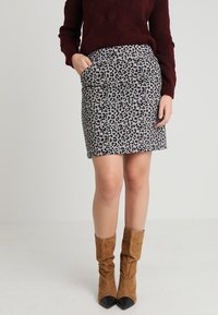 Falda de estampado de leopardo en tejido gris y negro, con un diseño ajustado y bolsillos laterales. Combinada con botas altas de ante marrones.