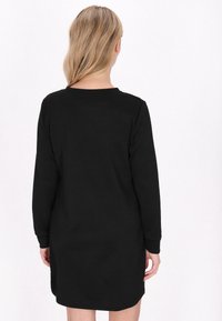 Schwarzes langärmeliges Kleid mit einem strukturierten Zickzackmuster, rundem Ausschnitt und lockerer Passform, das hinten bis zur Mitte des Oberschenkels reicht.