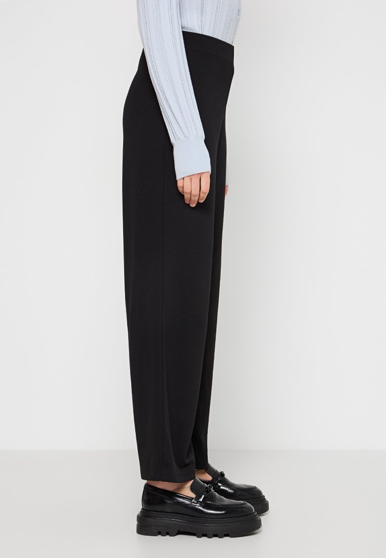 Pantaloni neri a vita alta con vestibilità dritta, texture liscia e cuciture sui lati; abbinati a un maglione a coste azzurro chiaro e scarpe nere.
