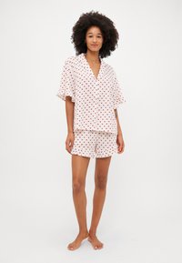 Ensemble de pyjama à manches courtes en tissu blanc avec des motifs de cœurs rouges, comprenant un haut à boutons et un short assorti avec des ourlets volants.
