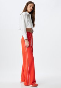Rode sweatpants met witte zijstreep, elastische tailleband en een relaxte fit, gecombineerd met een cropped wit overhemd met knopen.