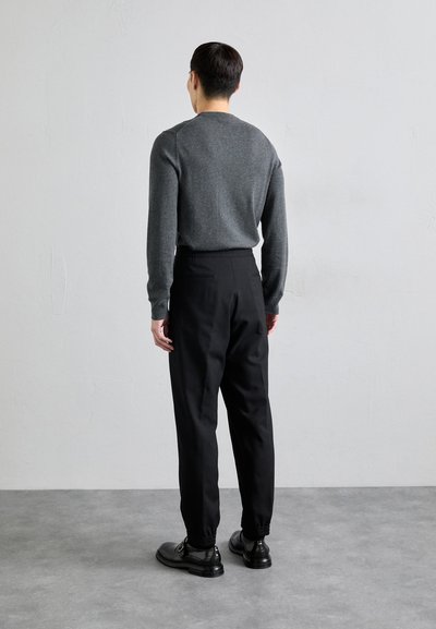 Suéter gris de manga larga combinado con pantalones negros de corte ajustado. Puños elásticos y cinturilla con cordones visibles en los pantalones. Zapatos negros completan el conjunto.