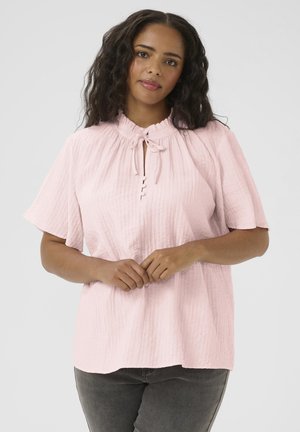 Blusa rosa chiaro realizzata in tessuto testurizzato, con un collo alto dotato di un nastro e una chiusura a bottoni sul davanti. Maniche corte.