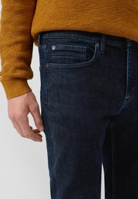Granatowe dżinsy o klasycznym kroju, delikatnym wyblaknięciu i standardowych kieszeniach. Uzupełnione o sweter z teksturowanej wełny w kolorze musztardowym.