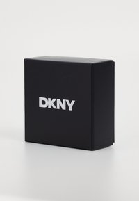 Scatola rettangolare nera con superficie opaca, con il logo bianco "DKNY" sul fronte. I bordi sono lisci e gli angoli sono arrotondati.