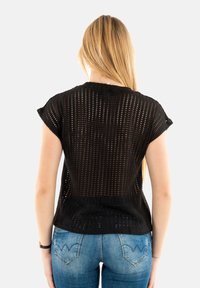 Haut en crochet noir à manches courtes avec une coupe loose, présentant une texture à motifs et un col rond, associé à un jean en denim bleu.