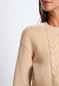 Maglione lavorato a maglia beige con motivo a trecce, colletto a coste e polsini, finitura testurizzata e vestibilità rilassata.