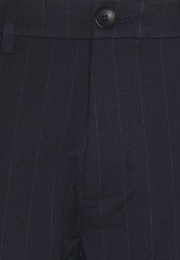 Pantalon bleu marine ajusté à fines rayures, réalisé en tissu texturé, avec une fermeture à bouton unique et une poche latérale.