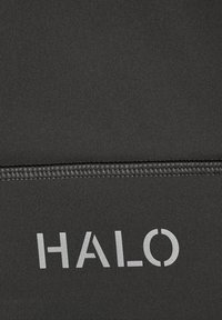 Close-up van zwart textiel met stikseldetail en het woord "HALO" gedrukt in grijze letters.