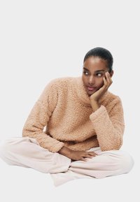 Lyserød, fluffy pullover med høj krave og lange ærmer, kombineret med løse, lyserøde bukser. Minimalistisk design, blød tekstur.