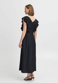 Marinblå klänning med rynkade ärmar, figursydd bodice och flödande kjol. Har en V-ringning i ryggen och ankel-lång design.