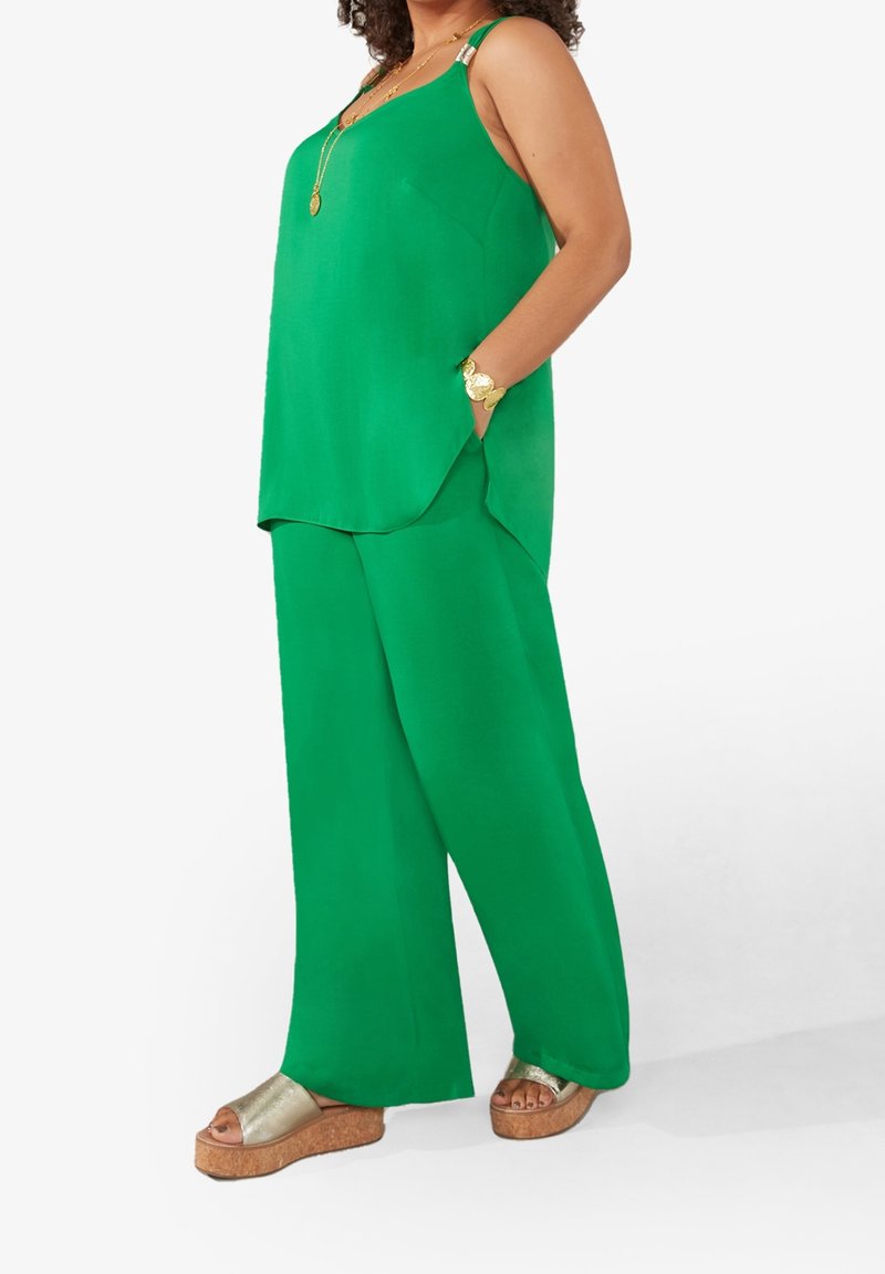 Grön ärmlös topp med en något rundad nederkant, i kombination med vida gröna byxor. Har metalliska detaljer och ett texturerat gyllene armband.
