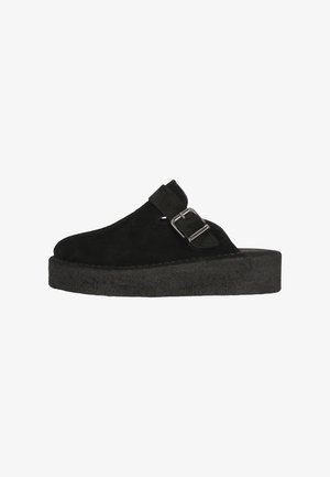 Sabots en suede noir avec une épaisse semelle plateforme, dotés d'une boucle latérale et d'un bout arrondi. Texture douce et design sobre.