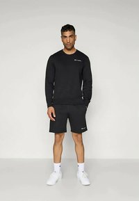 Zwarte sweatshirt en shorts van een zachte stof, met een subtiele logo op de borst, gecombineerd met witte sneakers en sportieve sokken.