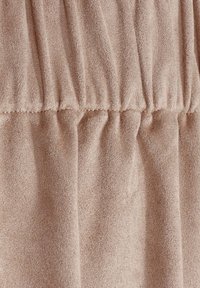 Tissu texturé brun clair avec un design froncé, comportant des plis et une surface douce et lisse. Les détails de couture sont visibles le long des bords.