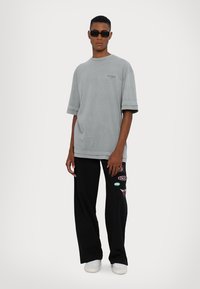 Grå oversized t-skjorte med korte ermer og rund hals, kombinert med svarte bukser med fargerike lapper og hvite joggesko.