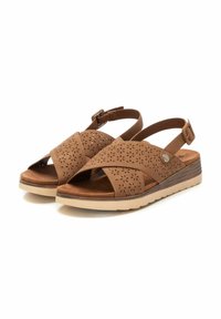 Sandalias de cuero marrón con un diseño floral recortado, correa ajustable en el tobillo y una suela de cuña baja con un fondo de goma de color claro.