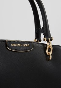 Czarna torebka ze skóry o teksturowanej powierzchni z detalem w postaci złotego łańcucha oraz plakietką z logo "MICHAEL KORS" umieszczoną przy podwójnych uchwytach.