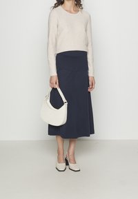 Pull en maille côtelée beige clair, jupe à panneaux bleu marine, sac épaule blanc et chaussures crème à talons carrés avec bout carré. Design simple et moderne.