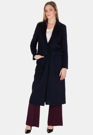 Cappotto lungo blu realizzato in tessuto misto lana, con colletto a punte, due tasche frontali e taglio dritto, abbinato a pantaloni bordeaux.