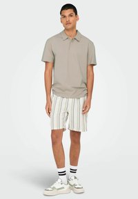 Lys grå polo skjorte med korte ærmer, kombineret med stribede shorts i beige, hvid og pastelfarver. Hvide sneakers med grønne accenter.