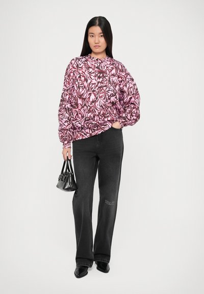 Sudadera de gran tamaño con estampado floral en rosa y burdeos, combinada con jeans de pierna ancha negros que tienen el bordado "STEGLITZ". Llevando un pequeño bolso negro.