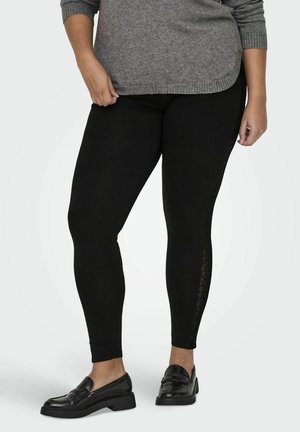 Svarta leggings med en texturerad spetsdetalj längs sidan, tillverkade av stretchigt material. Kombinerat med en grå tröja och svarta loafers.