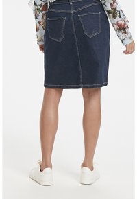 Denimkjol i mörkblå med kontrasterande vit söm, medellång, med två bakfickor och bärs med vita sneakers.