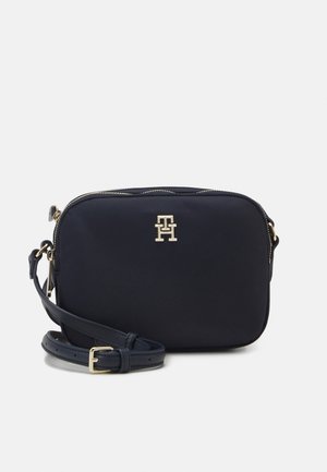 Kleine zwarte rechthoekige crossbodytas met gouden TH-logo en verstelbare band op een lichte achtergrond.