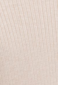 Gros plan sur un tissu en maille côtelée beige avec des lignes verticales texturées et un motif tissé doux.