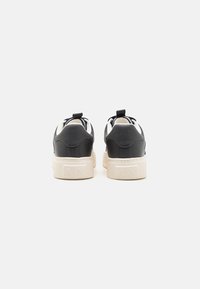 Sorte lærersneakers med en hvit gummisåle, med en teksturert hæl og en liten løfteløkke bak for enkel påkledning.