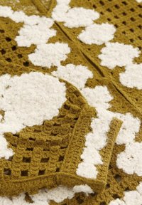 Indumento all'uncinetto con una base gialla senape e motivi floreali bianchi, finitura testurizzata e design a maglia aperta.