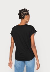 T-shirt nera a maniche corte in tessuto morbido, con vestibilità rilassata e scollo arrotondato, abbinata a jeans azzurri.