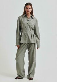 Cămașă verde deschis, cu butoni, cu pliuri; asortată cu pantaloni largi. Ambele sunt realizate dintr-un material neted, având mâneci lungi.