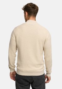 Beige strikket sweater med rund hals, ribbede manchetter og kant. Har tekstureret stof og et glat design bagpå.