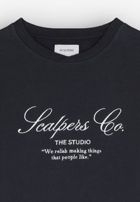 Tricou din bumbac de culoare bleumarin, cu guler rotund, având text brodat alb: "Scalpers Co. THE STUDIO" și un slogan dedesubt.