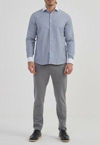 Chemise à rayures à manches longues bleue et blanche, dotée d'un col pointu, d'une fermeture à boutons et de poignets blancs contrastants, associée à un pantalon gris.
