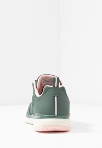 Grön sportskor med ovandel i nät, rosa inredning och vit sula. Anmärkningsvärda detaljer inkluderar en randig accent på hälen och en logotyp.