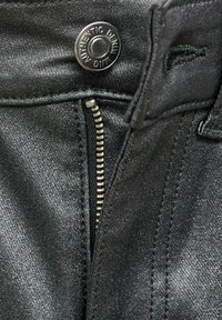 Mustat farkut, joissa on metallinen kiilto, vetoketjukiinnitys ja painonappi, jossa on teksti "AUTHENTIC DENIM". Suorat ompelusaumat.