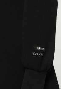 Crna majica dugih rukava s logom "Armani Exchange" i otisnutim tekstom blizu manžeta na tkanini.