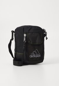 Svart tygväska med meshficka, gul sömnad, dragkedjestängning och justerbar rem. Har en Adidas-logga på framsidan.