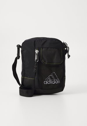 Must mustriga kott, millel on silmale nähtav tasku, kollane tikand, tõmblukuga sulgur ja reguleeritav rihm. Ees on Adidas'i logo.