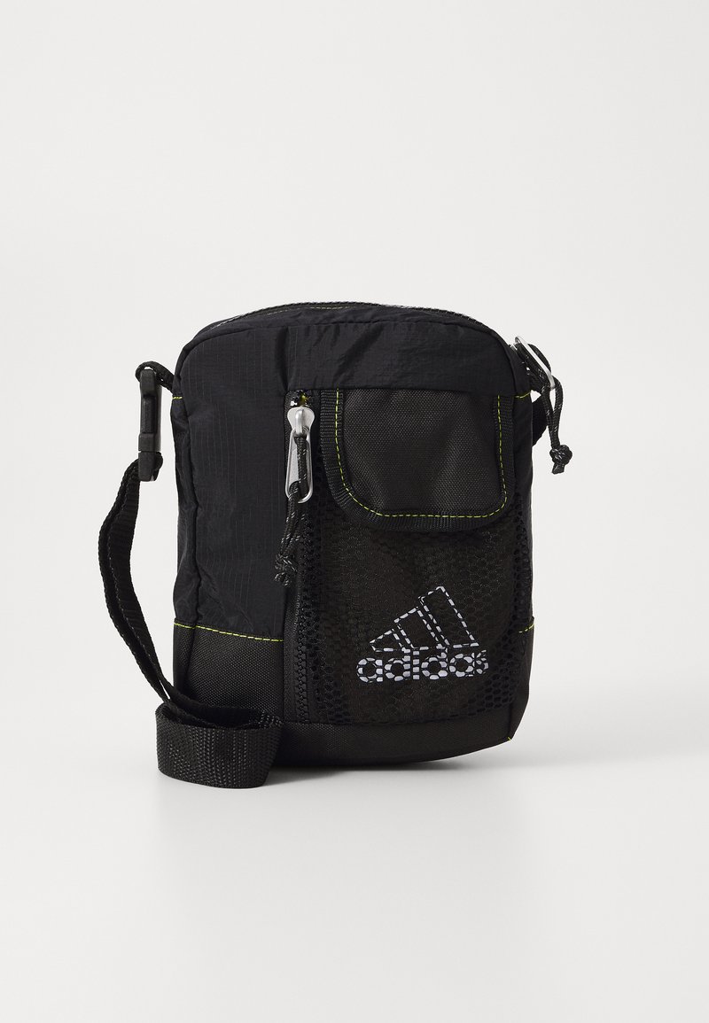 Svart tygväska med meshficka, gul sömnad, dragkedjestängning och justerbar rem. Har en Adidas-logga på framsidan.