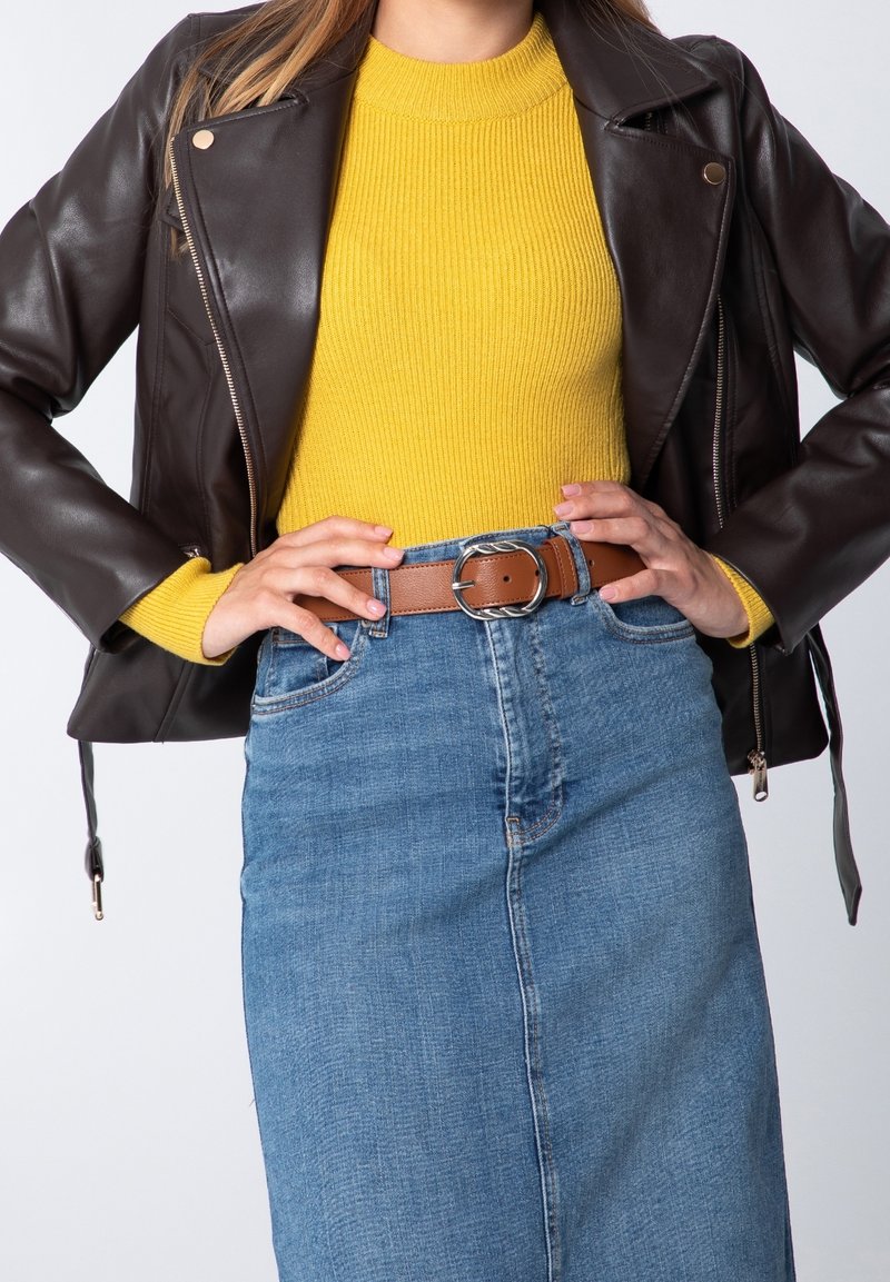 Ruskea nahkainen moottoripyörätakki, keltainen ribbineulepusero, farkkuhame. Ruskea vyö hopeisella soljella. Istuva malli, rento look.