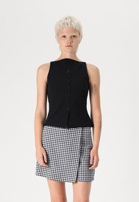 Čierny top bez rukávov s okrúhlym výstrihom a prednými gombíkmi, skombinovaný s sukňou v houndstooth vzore v čierno-bielej farbe.