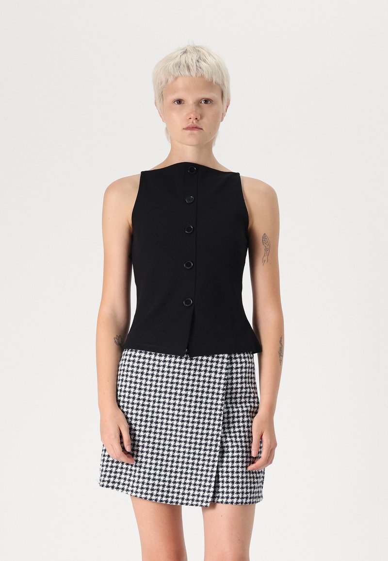 Čierny top bez rukávov s okrúhlym výstrihom a prednými gombíkmi, skombinovaný s sukňou v houndstooth vzore v čierno-bielej farbe.