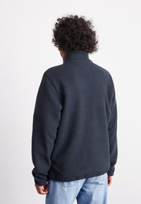 Bluza polarowa w kolorze ciemnogranatowym z wysokim kołnierzem i długimi rękawami; charakteryzuje się miękką, teksturowaną powierzchnią i prostym dołem.