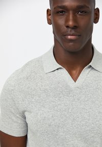 Ljust grått stickat pikétröja med V-halsringning och korta ärmar, som har en subtil textur och ribbade mudddetaljer.