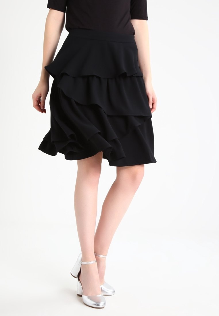 Svart lager-på-lager volangkjol i lättviktig tyg, med flera lager, i kombination med glänsande silvriga högklackade skor.